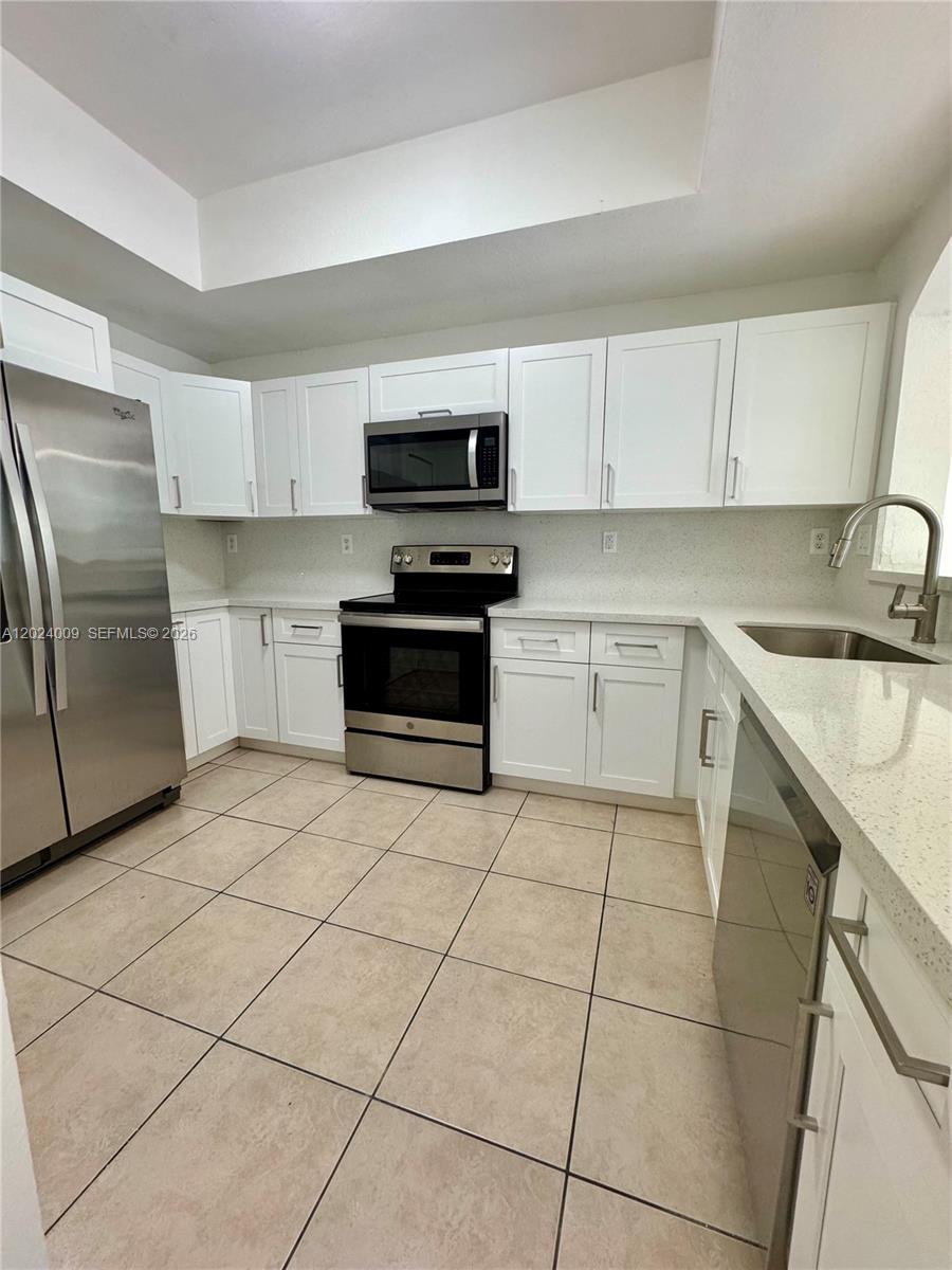 A kitchen features white cabinets, stainless steel appliances, and light-colored countertops and floor tiles — 8936 W Flagler St # 201, Miami FL 33174, MIAMI, FL