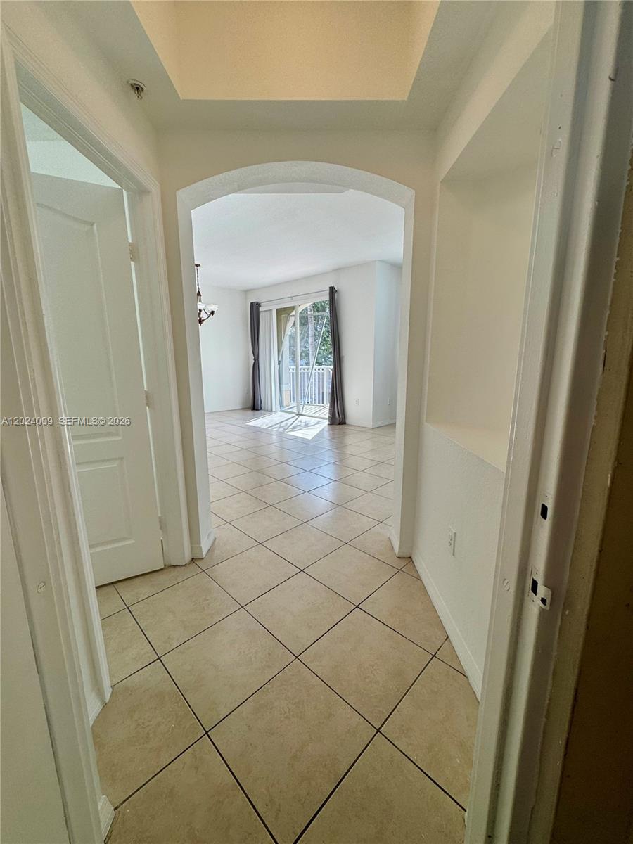 A tiled hallway leads through an arched doorway into a bright living area with balcony access — 8936 W Flagler St # 201, Miami FL 33174, MIAMI, FL