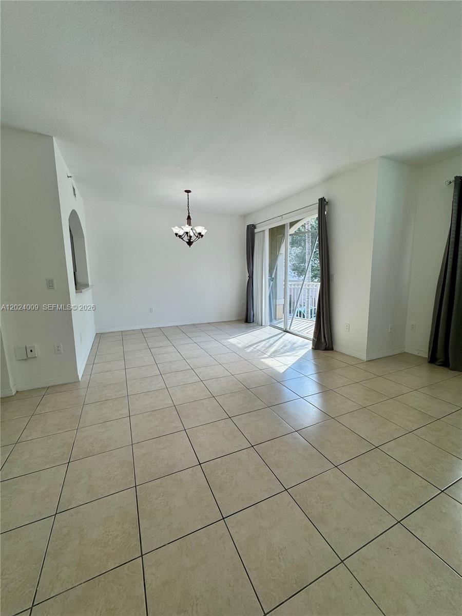 A bright, empty living room features beige tile flooring, a chandelier, and a sliding glass door — 8936 W Flagler St # 201, Miami FL 33174, MIAMI, FL