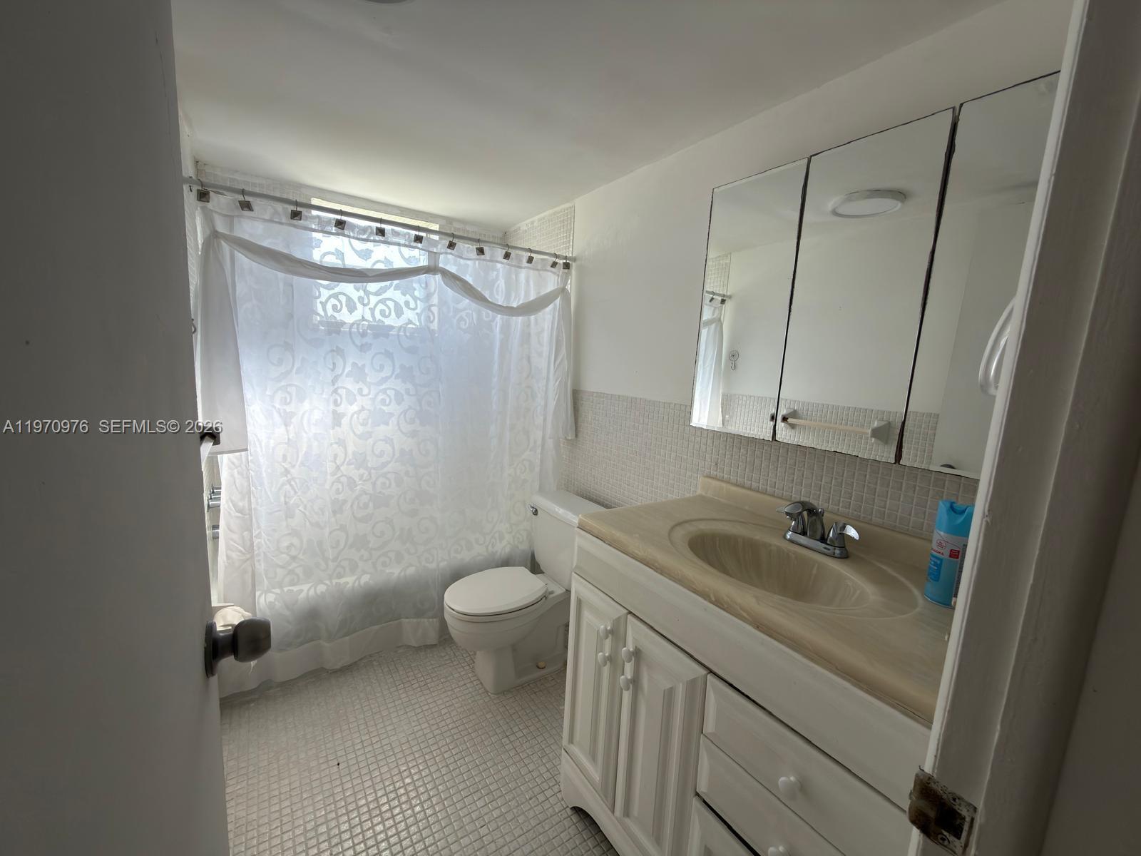 A bathroom features a white vanity, a toilet, and a shower with a patterned curtain — 30 SE 4th Ave # 103, Hallandale Beach FL 33009, HALLANDALE BEACH, FL