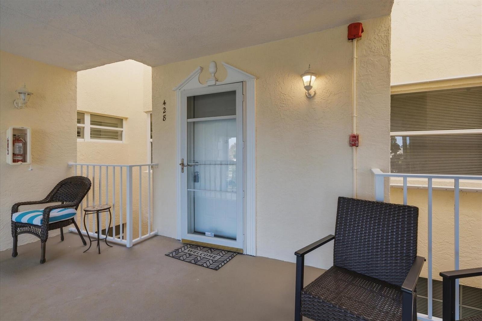 An outdoor balcony features two wicker chairs, a small table, and a front door — 428 Grove Isle Circle # 9, Vero Beach FL 32962, VERO BEACH, FL