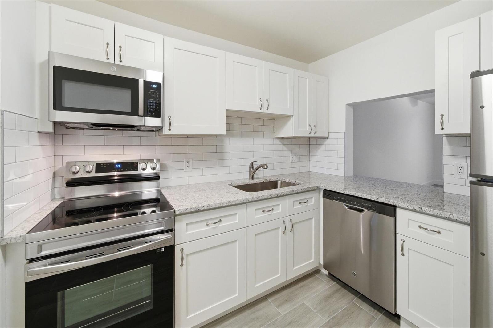 A kitchen features white cabinets, granite countertops, stainless steel appliances, and a subway tile backsplash — 428 Grove Isle Circle # 9, Vero Beach FL 32962, VERO BEACH, FL