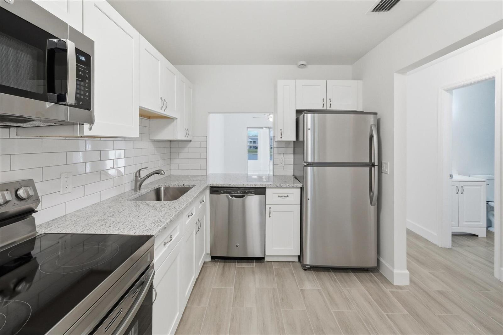 A kitchen features white cabinets, granite countertops, stainless steel appliances, and light wood-look tile flooring — 428 Grove Isle Circle # 9, Vero Beach FL 32962, VERO BEACH, FL
