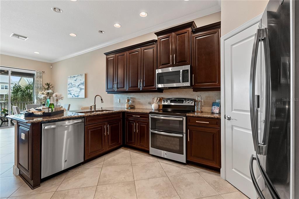 A kitchen features dark wood cabinets, granite countertops, stainless steel appliances, and tile flooring — 6043 ANCHORAGE WAY S, ST PETERSBURG, FL