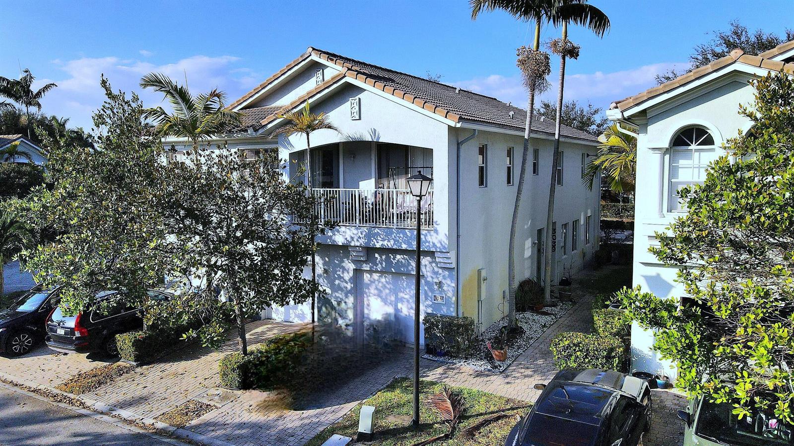 An exterior view of a two-story light-colored house with a balcony and paved driveway — 3037 Laurel Ridge Circle, Riviera Beach FL 33404, RIVIERA BEACH, FL