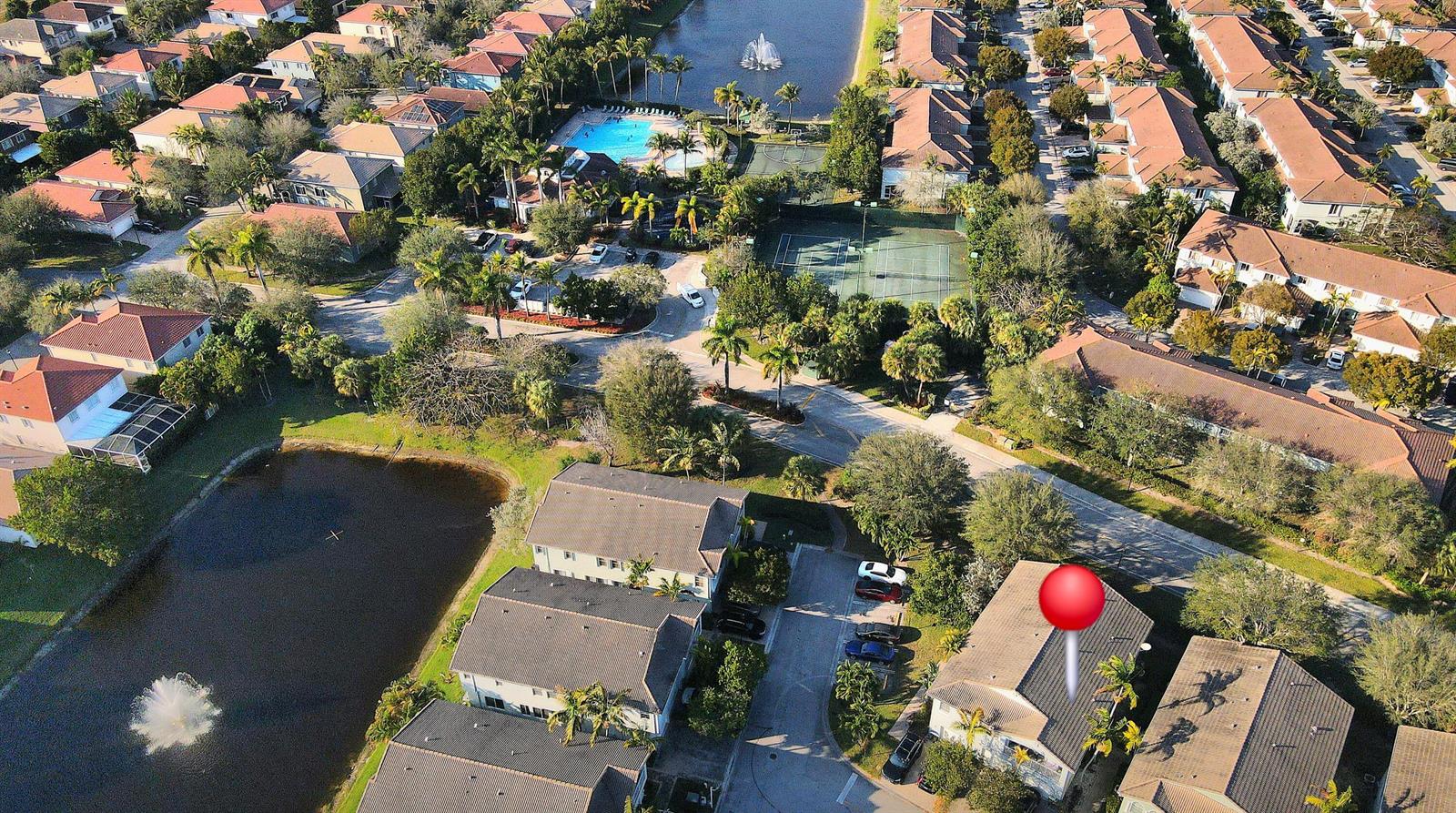 An aerial view shows a residential neighborhood with houses, a lake, and a tennis court — 3037 Laurel Ridge Circle, Riviera Beach FL 33404, RIVIERA BEACH, FL