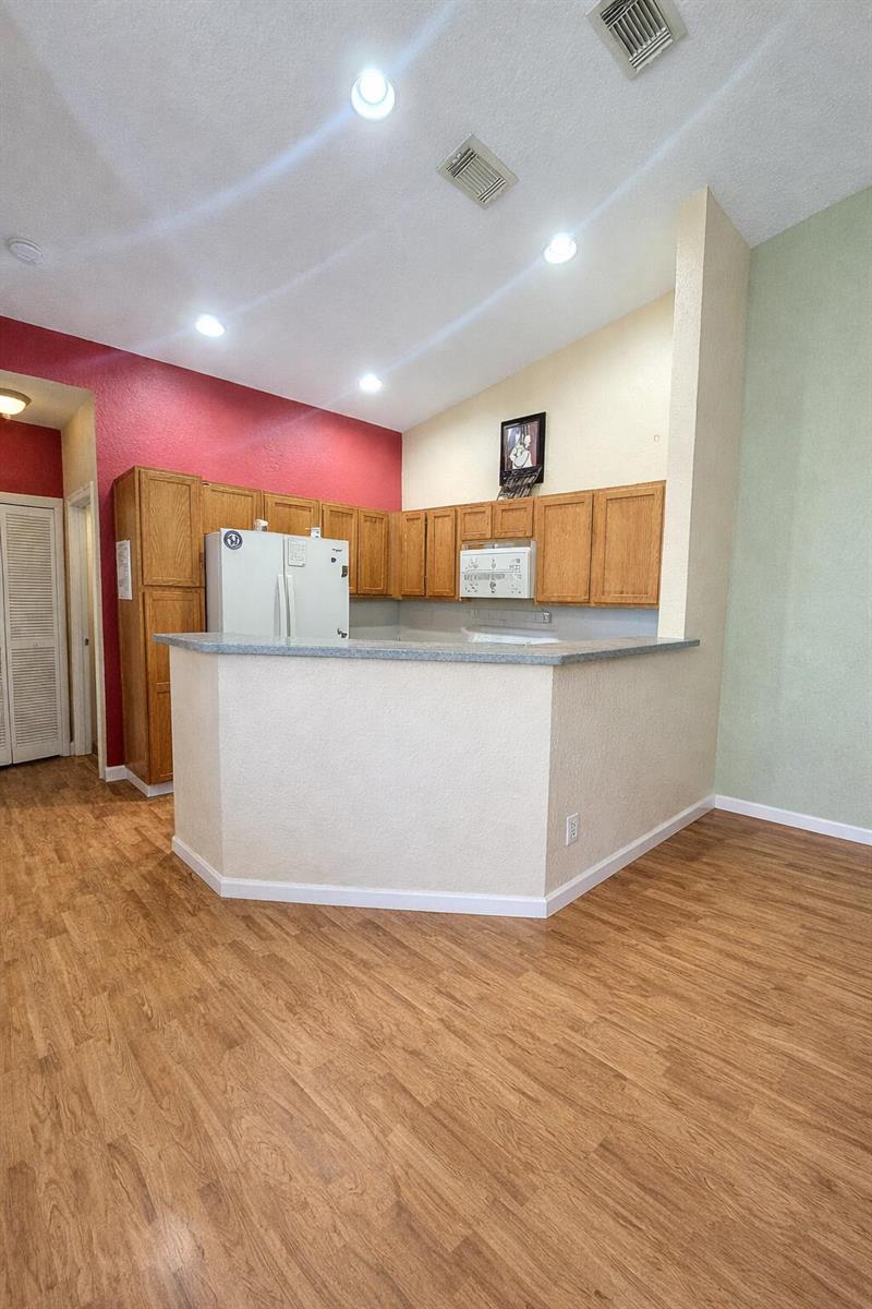 A kitchen features wood cabinets, a white refrigerator, and a breakfast bar with laminate countertops — 3037 Laurel Ridge Circle, Riviera Beach FL 33404, RIVIERA BEACH, FL