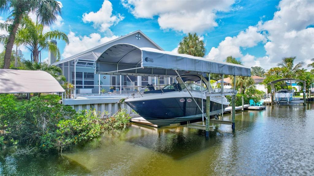 A boat on a lift sits in a canal behind a house with a pool — 360 46TH COURT E, BRADENTON, FL