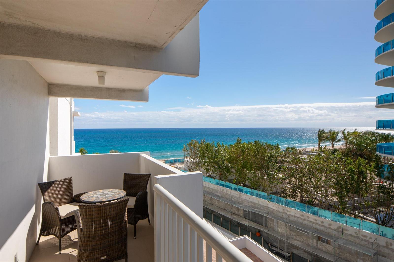 A balcony with wicker furniture overlooks the ocean and a construction site below — 1370 S Ocean Boulevard # 604, Pompano Beach FL 33062, POMPANO BEACH, FL