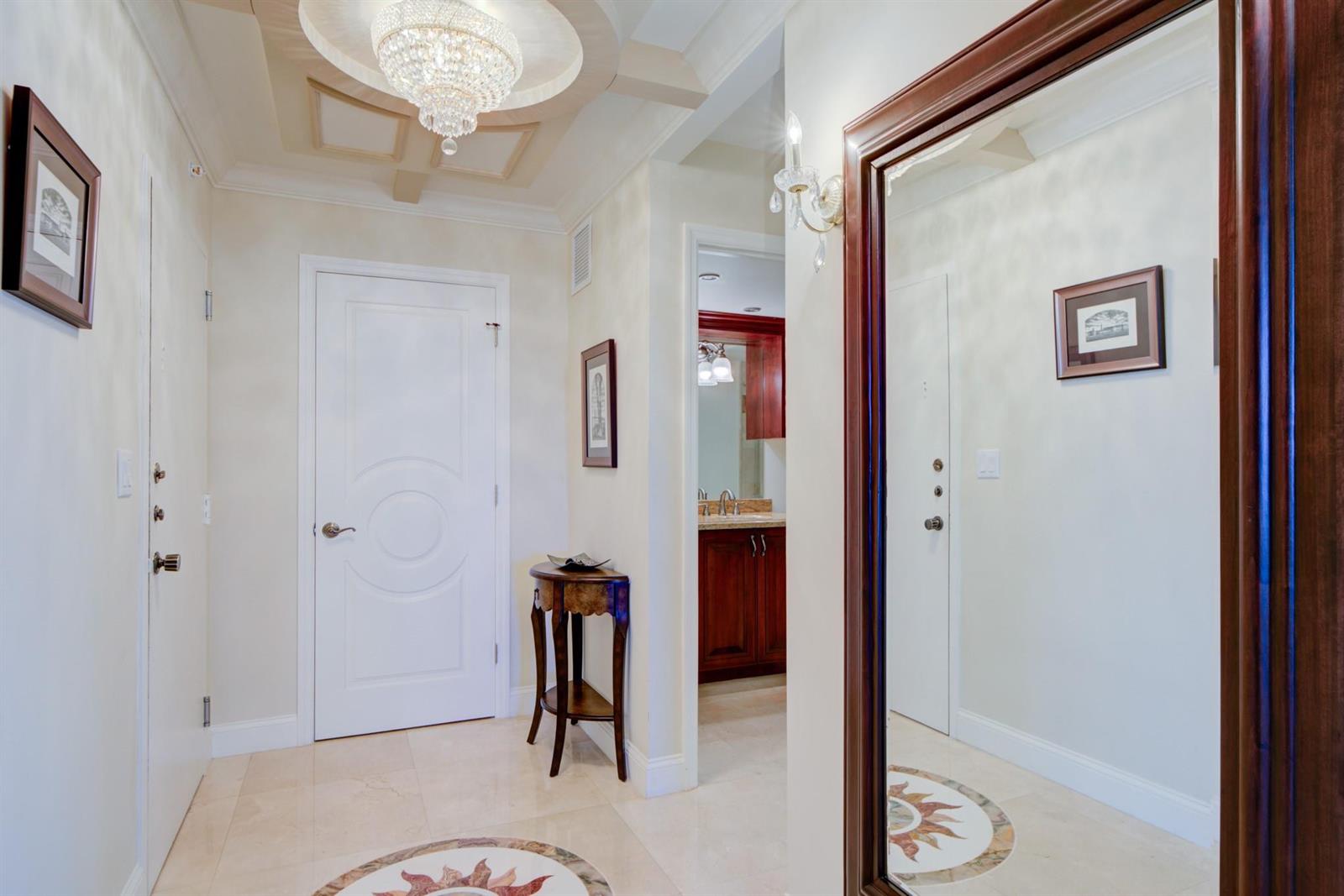 A foyer features a crystal chandelier, a large mirror, a small table, and tile flooring — 1370 S Ocean Boulevard # 604, Pompano Beach FL 33062, POMPANO BEACH, FL