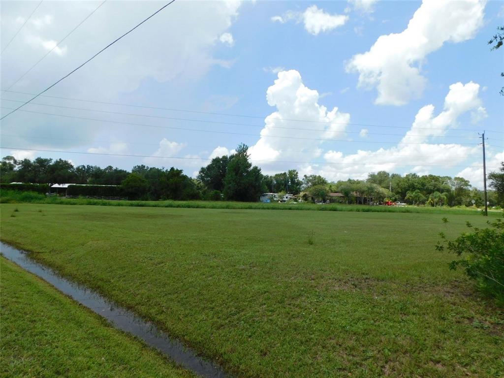 A wide, grassy vacant lot features a drainage ditch in the foreground under a cloudy sky — 10099 SW KISSIMMEE ROAD, ARCADIA, FL
