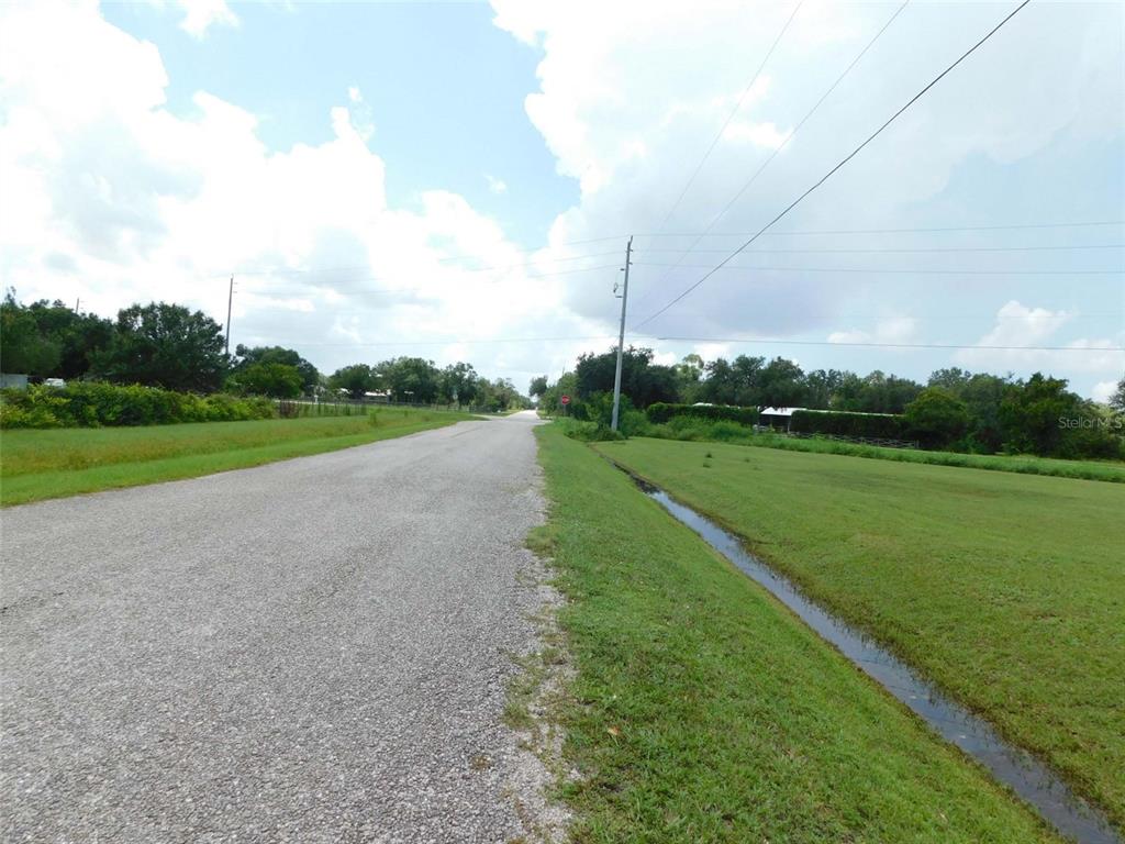 A paved road stretches into the distance past grassy fields and a drainage ditch — 10099 SW KISSIMMEE ROAD, ARCADIA, FL