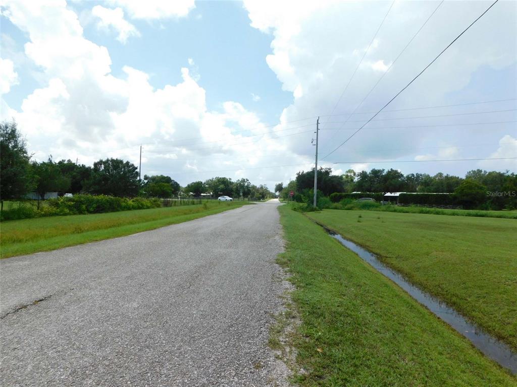 A paved road stretches into the distance past grassy fields and a drainage ditch — 10099 SW KISSIMMEE ROAD, ARCADIA, FL