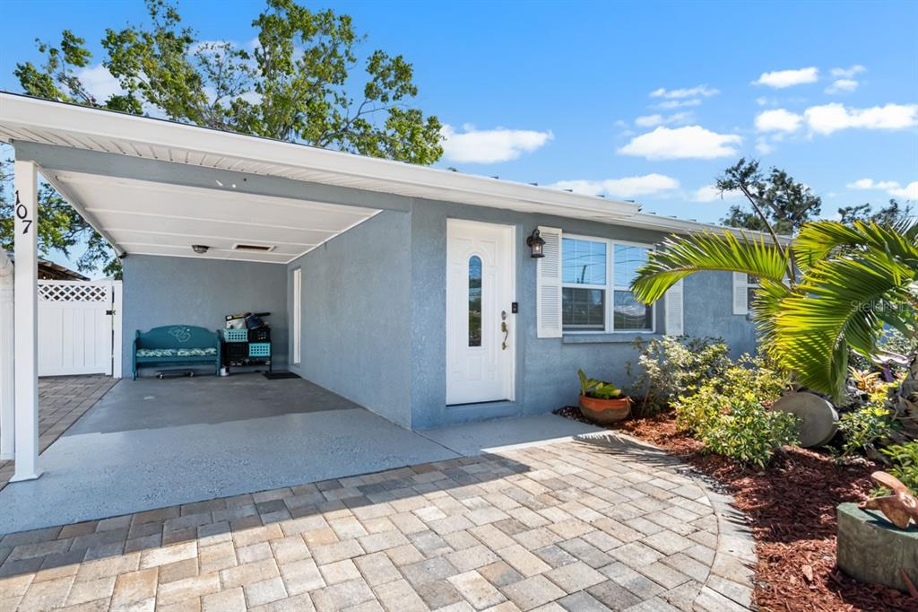 A blue house exterior features a covered carport, a white front door, and paver driveway — 107 6TH STREET NW, RUSKIN, FL