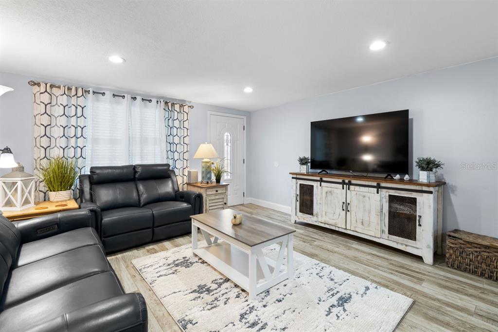 A living room features light gray walls, wood-look flooring, black leather furniture, and a television console — 107 6TH STREET NW, RUSKIN, FL