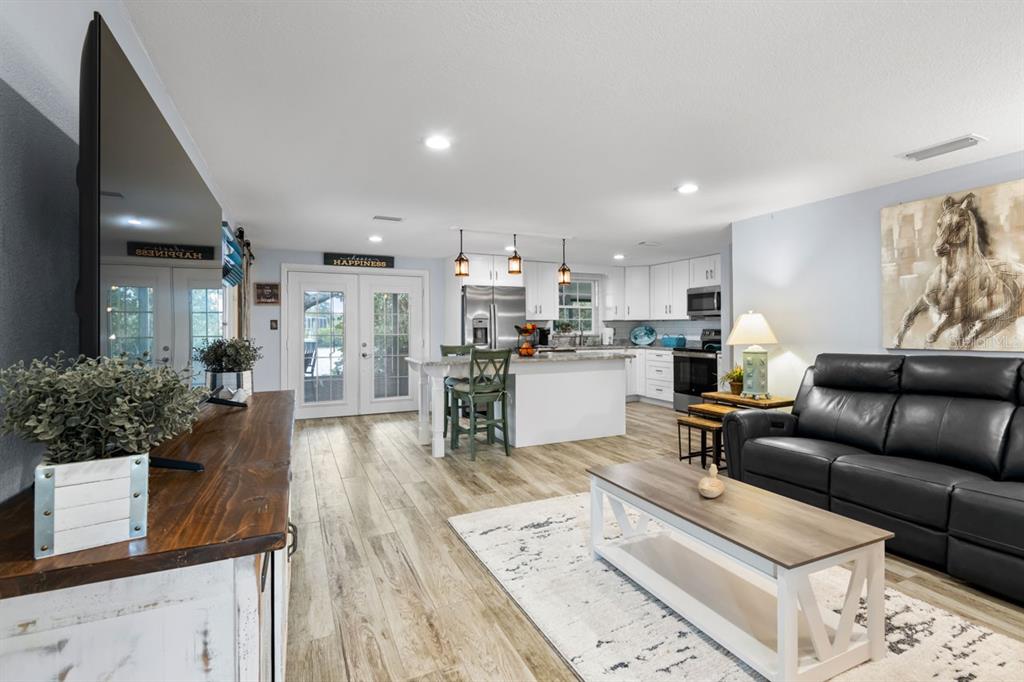 An open-concept living room and kitchen featuring wood-look flooring, a black leather sofa, and island — 107 6TH STREET NW, RUSKIN, FL