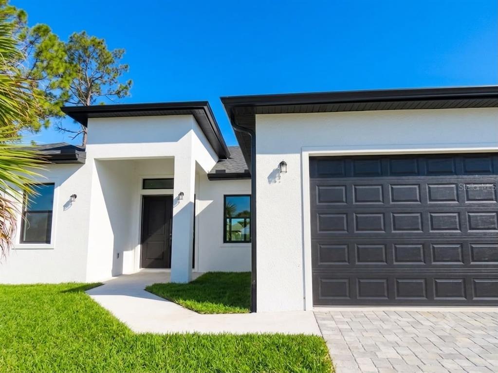 A modern white house exterior features a black garage door and a recessed front entrance — 2651 PEAKE STREET, NORTH PORT, FL