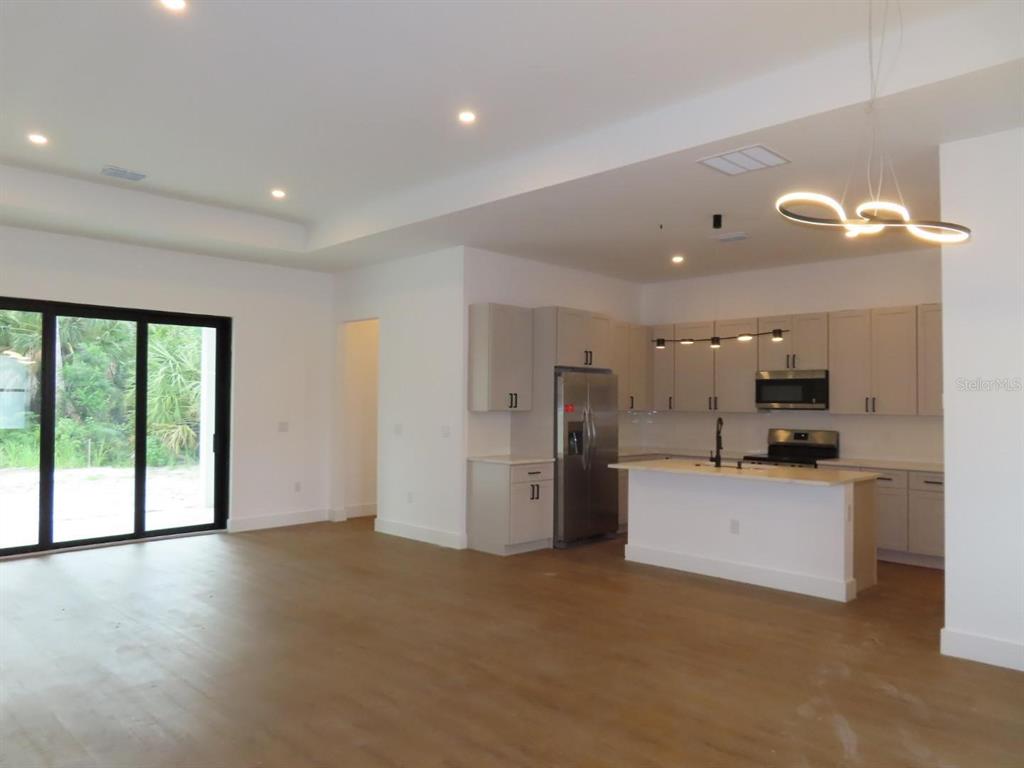 An open-concept kitchen and living area features light wood floors, gray cabinetry, and sliding doors — 2651 PEAKE STREET, NORTH PORT, FL