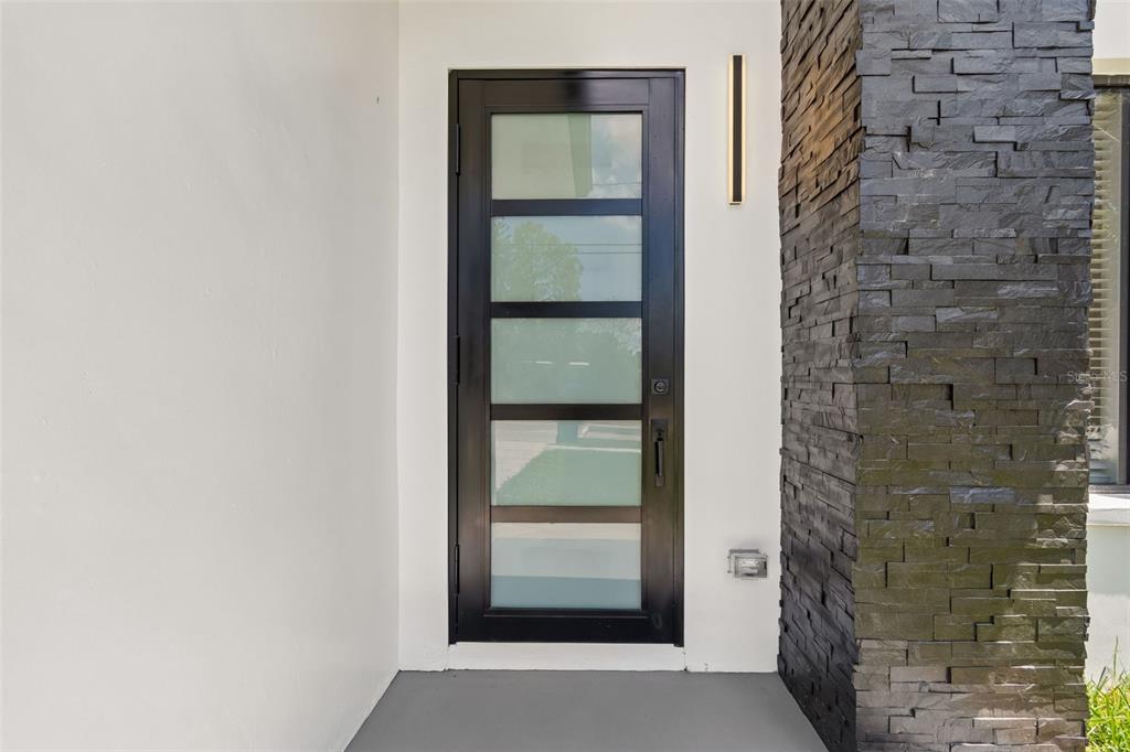 A modern black-framed front door with frosted glass panels sits beside a dark stone pillar — 4101 W MANGO AVENUE, TAMPA, FL