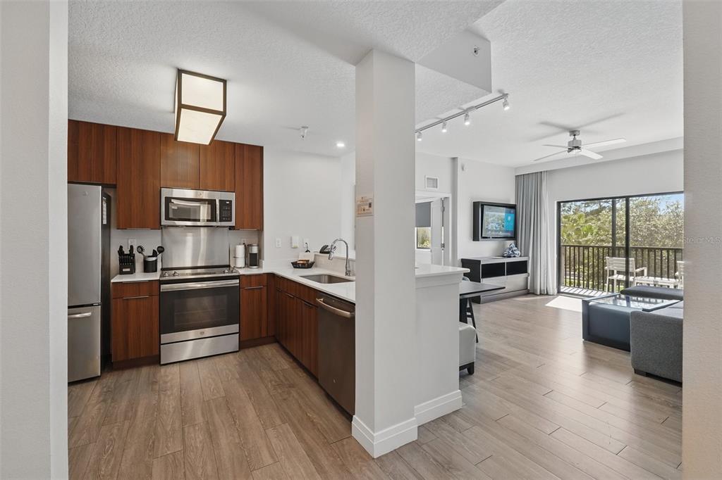 A modern kitchen with wood cabinets and stainless steel appliances opens into a living area — 14501 GROVE RESORT AVENUE UNIT 2232, WINTER GARDEN, FL
