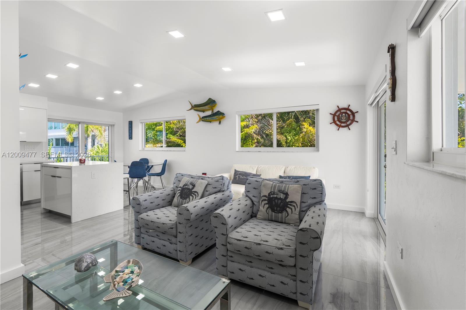 A living room with gray patterned armchairs, a glass coffee table, and white kitchen cabinets — 200 Plantation Shores Dr, Tavernier FL 33070, TAVERNIER, FL