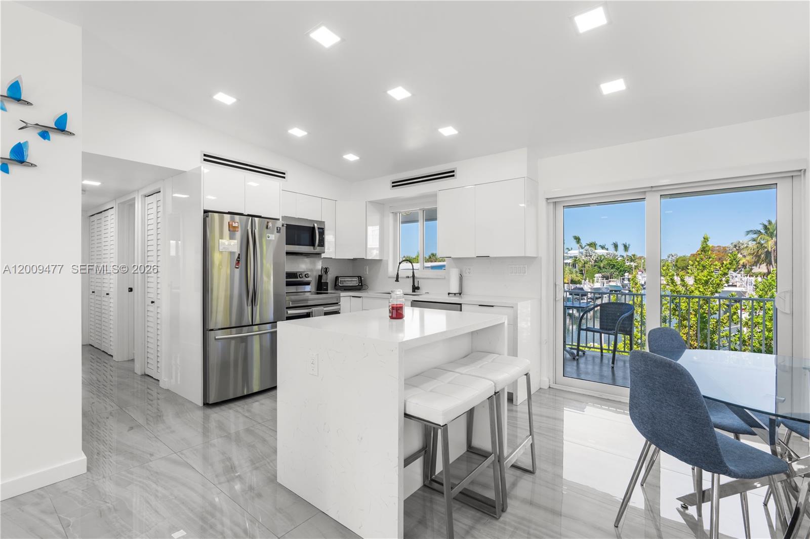 A modern white kitchen features a central island, stainless steel appliances, and a balcony view — 200 Plantation Shores Dr, Tavernier FL 33070, TAVERNIER, FL