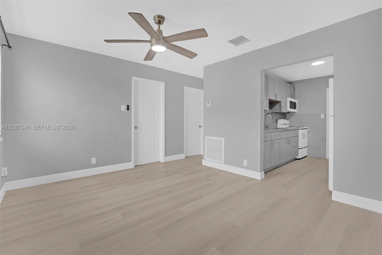A living area with light wood flooring, gray walls, and an adjacent kitchen — 369 Phippen Waiters Rd # 1, Dania Beach FL 33004, DANIA BEACH, FL