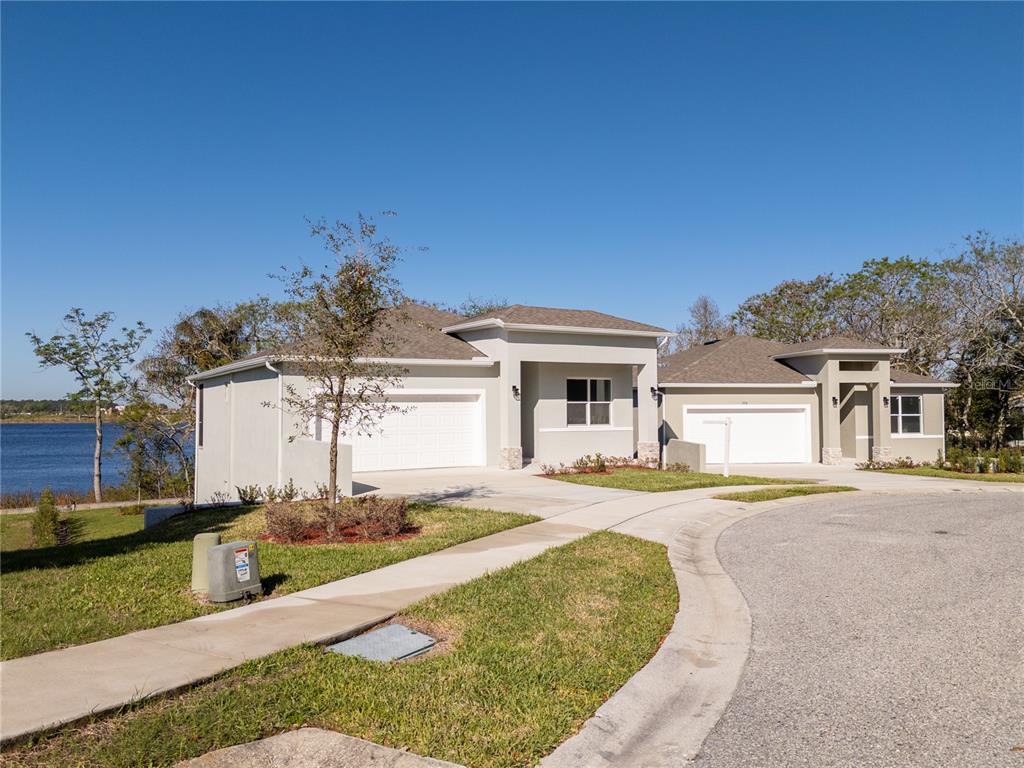Two modern single-story houses with attached garages sit along a curved street near a lake — 356 CHEROKEE AVENUE, HAINES CITY, FL