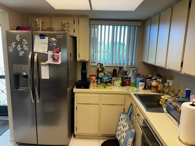 A kitchen features a stainless steel refrigerator, light-colored cabinets, and a window with vertical blinds — 3186 Via Poinciana # 306, FL 33467, FL