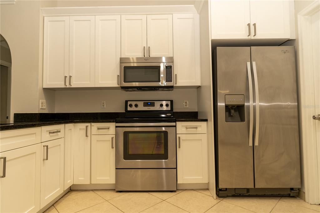 A kitchen features white cabinets, stainless steel appliances, and dark countertops over tiled flooring — 11547 GRAZELEY COURT, ORLANDO, FL