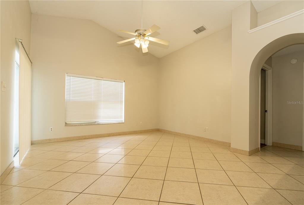 An empty room with beige tile flooring, a vaulted ceiling, and a ceiling fan — 11547 GRAZELEY COURT, ORLANDO, FL