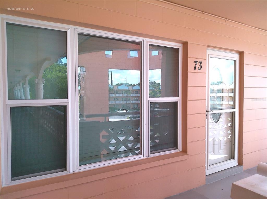 A view of a building exterior featuring a glass door labeled 73 and windows — 2457 ECUADORIAN WAY UNIT 73, CLEARWATER, FL