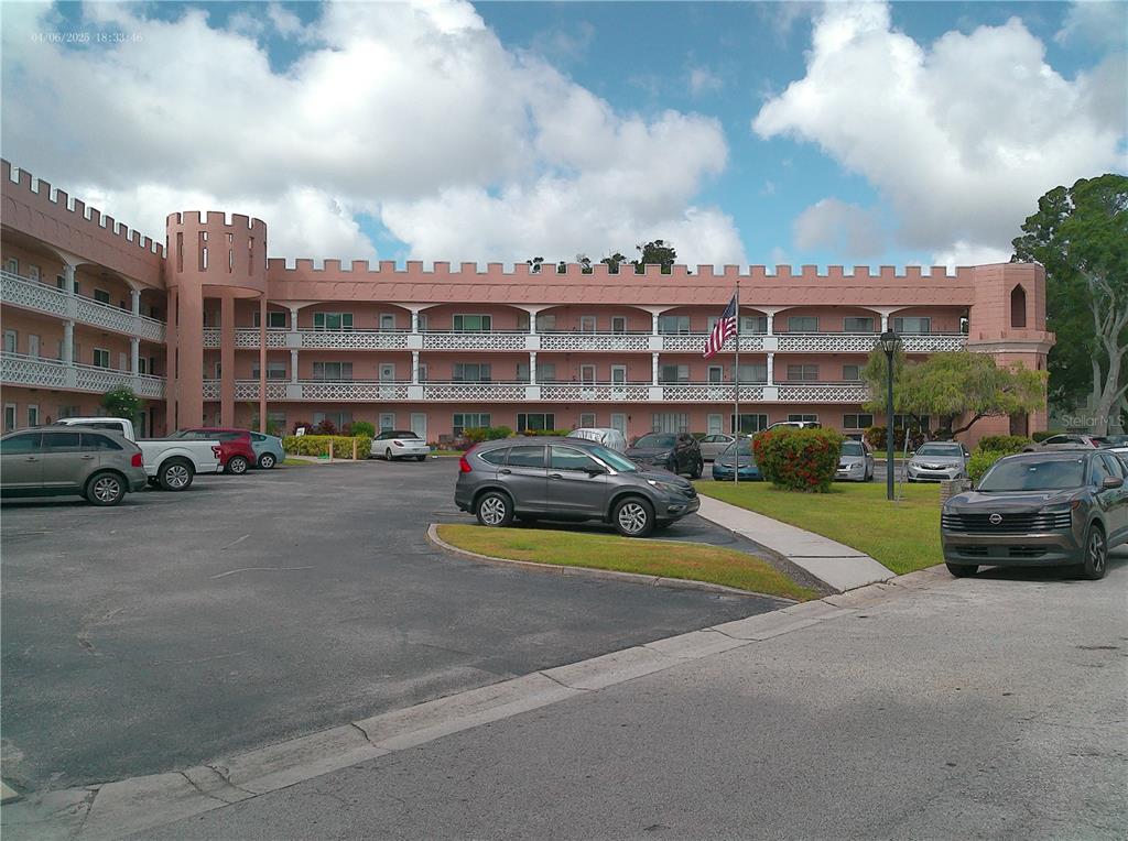 A three-story pink apartment building with castle-like battlements and a parking lot in front — 2457 ECUADORIAN WAY UNIT 73, CLEARWATER, FL