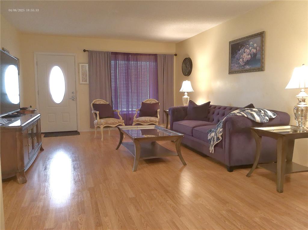 A living room features a purple sofa, two accent chairs, a coffee table, and wood flooring — 2457 ECUADORIAN WAY UNIT 73, CLEARWATER, FL