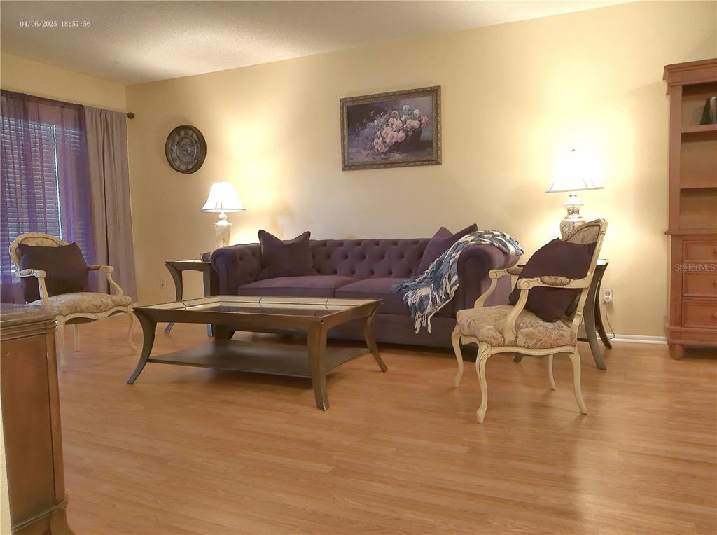 A living room features a purple tufted sofa, two patterned chairs, and light wood flooring — 2457 ECUADORIAN WAY UNIT 73, CLEARWATER, FL