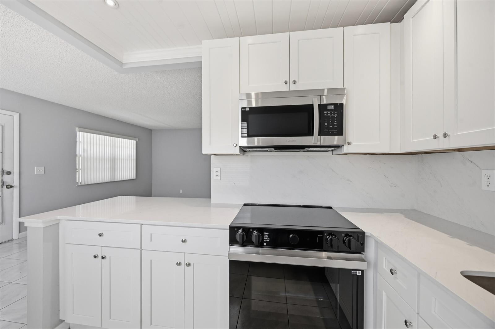 A kitchen features white cabinets, a stainless steel microwave, a black stove, and white countertops — 422 Burgundy I, Delray Beach FL 33484, DELRAY BEACH, FL