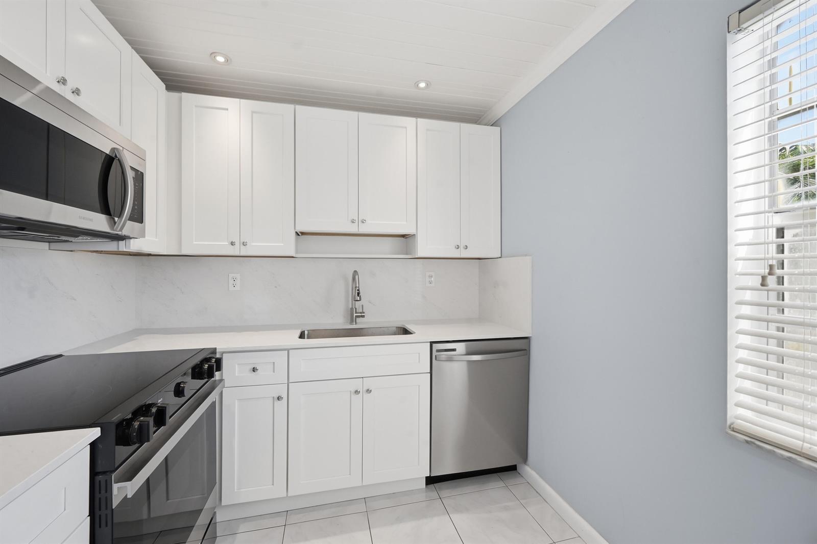 A kitchen features white cabinets, stainless steel appliances, a marble-look backsplash, and light-colored tile flooring — 422 Burgundy I, Delray Beach FL 33484, DELRAY BEACH, FL