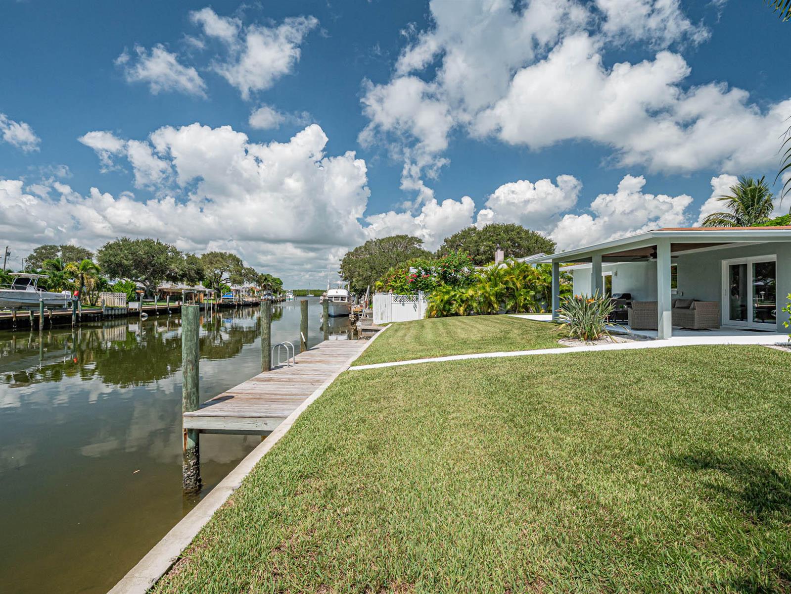 A grassy backyard features a wooden boat dock extending into a canal beside a house — 255 Marina Drive, Fort Pierce FL 34949, FORT PIERCE, FL