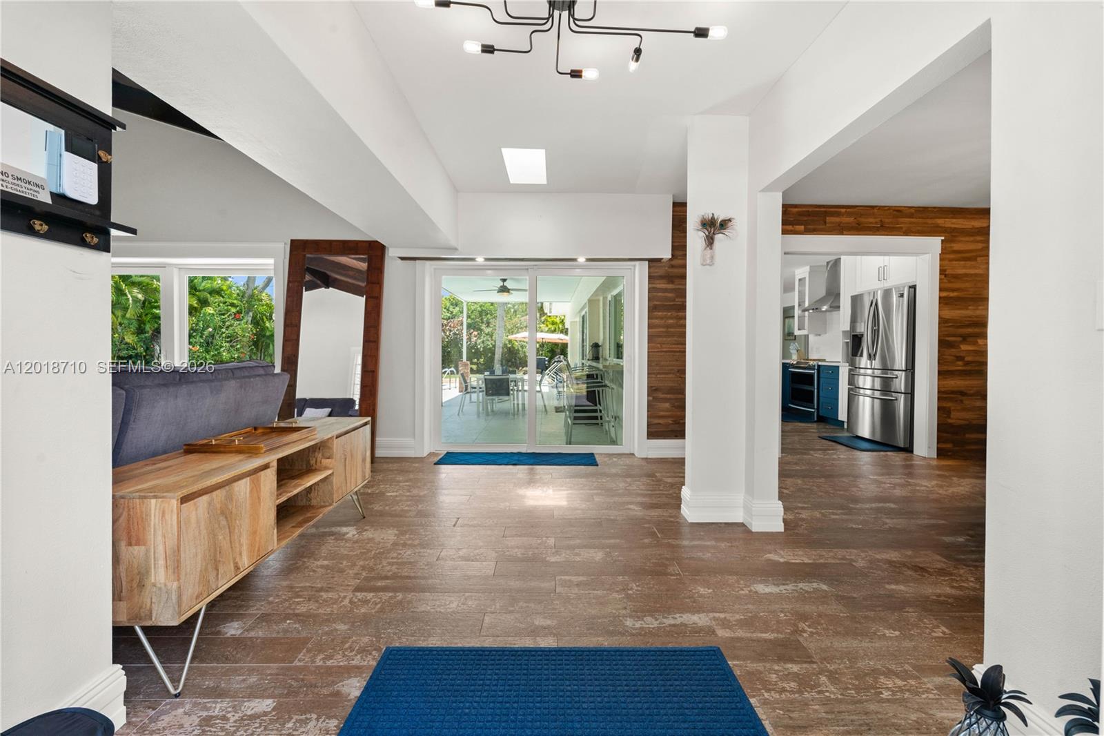 A living area with wood-look tile floors leads to a sliding glass door and kitchen — 8380 SW 186 St, Cutler Bay FL 33157, CUTLER BAY, FL