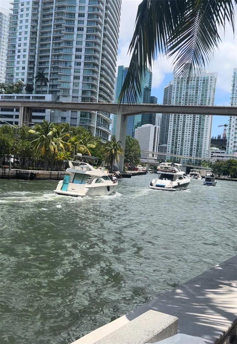 Several boats travel along a canal lined with tall buildings and an overhead bridge — 185 SW 7 ST # 1802, Miami FL 33130, MIAMI, FL