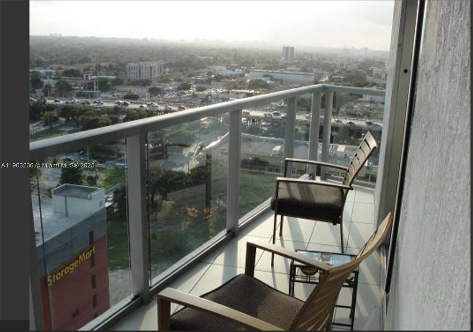 A balcony with two chairs overlooks a city landscape with a nearby storage facility — 185 SW 7 ST # 1802, Miami FL 33130, MIAMI, FL