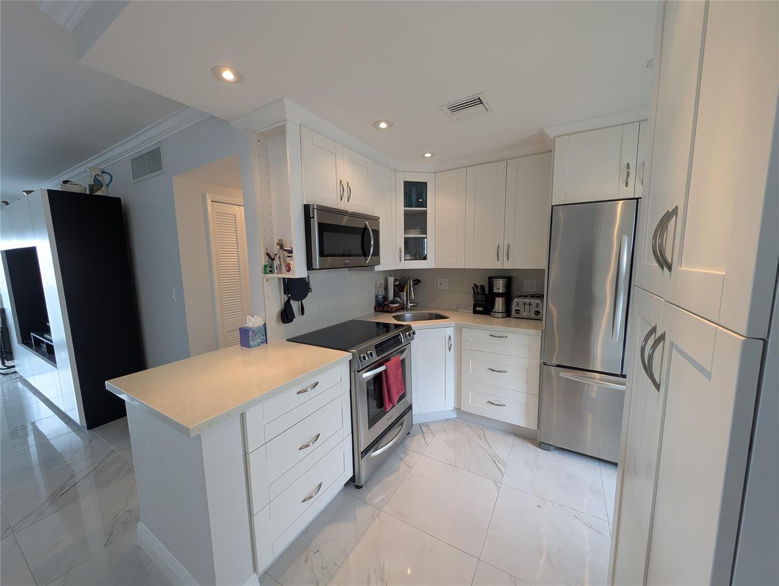 A modern kitchen features white cabinetry, stainless steel appliances, and light-colored stone countertops — 3209 S Ocean Drive # 4E, Hallandale Beach FL 33009, HALLANDALE BEACH, FL