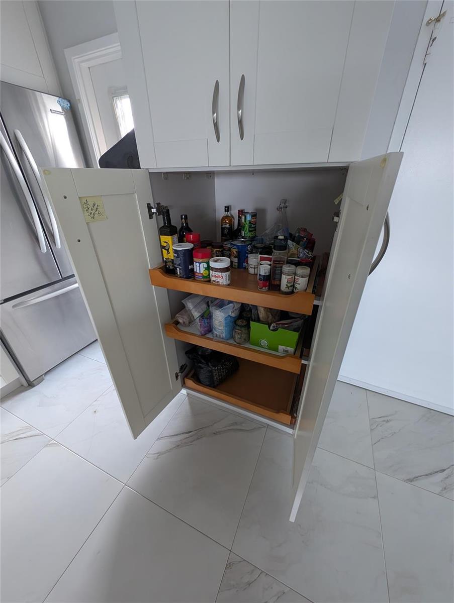 A white kitchen pantry cabinet with pull-out shelves stands next to a stainless steel refrigerator — 3209 S Ocean Drive # 4E, Hallandale Beach FL 33009, HALLANDALE BEACH, FL
