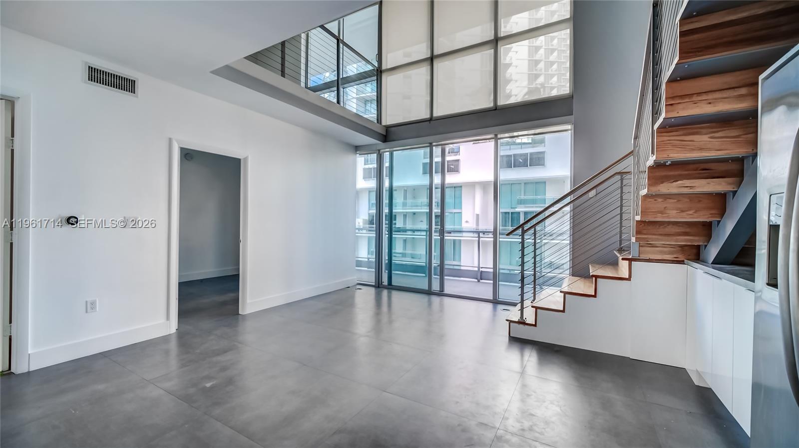 A modern living room features concrete floors, a floating staircase, and floor-to-ceiling windows — 90 SW 3rd St, Miami FL 33130, MIAMI, FL
