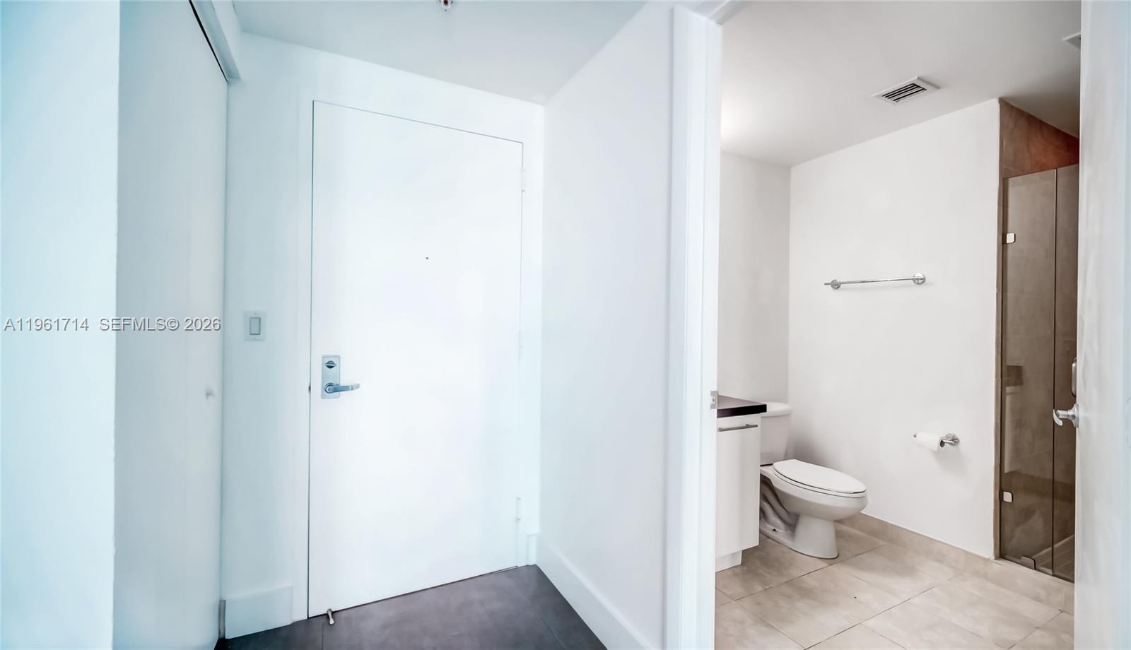 A white door opens into a bathroom featuring a toilet, vanity, and glass-enclosed shower — 90 SW 3rd St, Miami FL 33130, MIAMI, FL