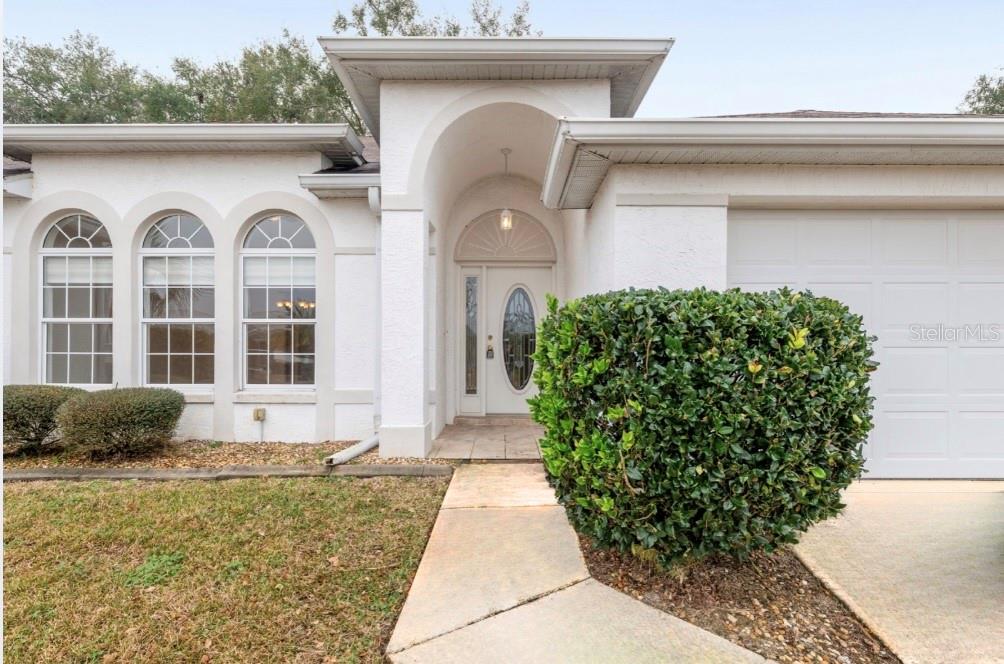 The exterior of a white house features an arched entryway, three arched windows, and landscaping — 5888 NW 21ST STREET, OCALA, FL