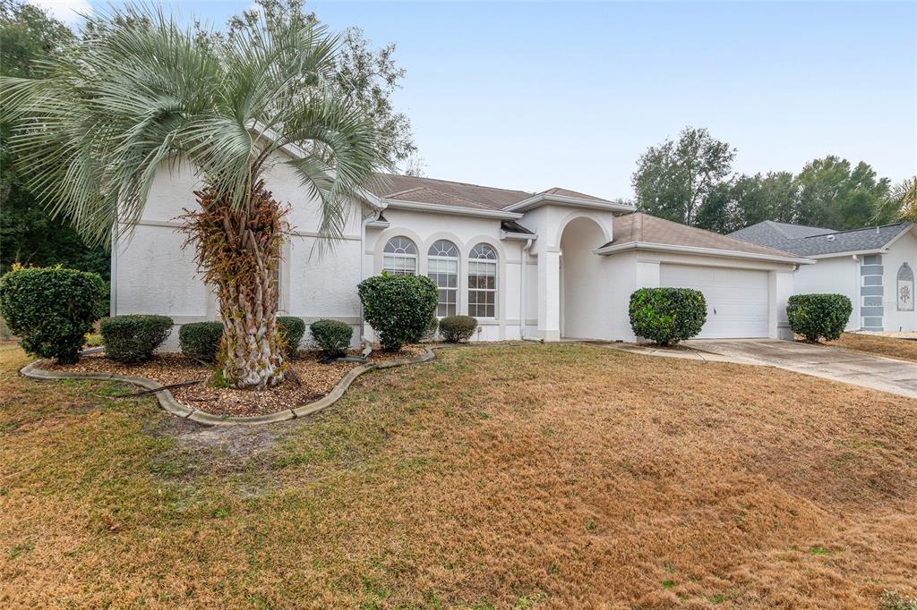 A single-story white stucco house features a palm tree, arched windows, and a two-car garage — 5888 NW 21ST STREET, OCALA, FL