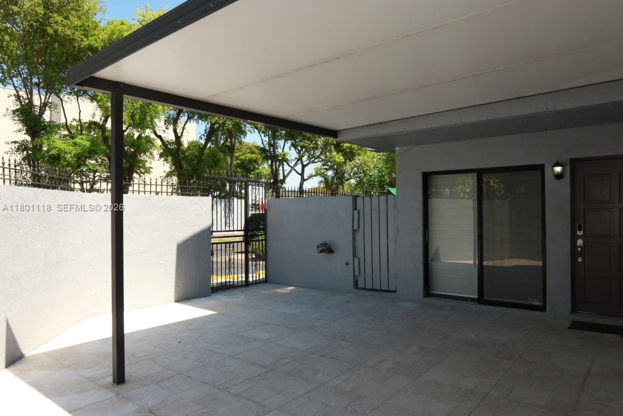 A covered patio area features light-colored floor tiles, a gray wall, and a metal gate — 8098 NW 99th Ter, Hialeah Gardens FL 33016, HIALEAH GARDENS, FL