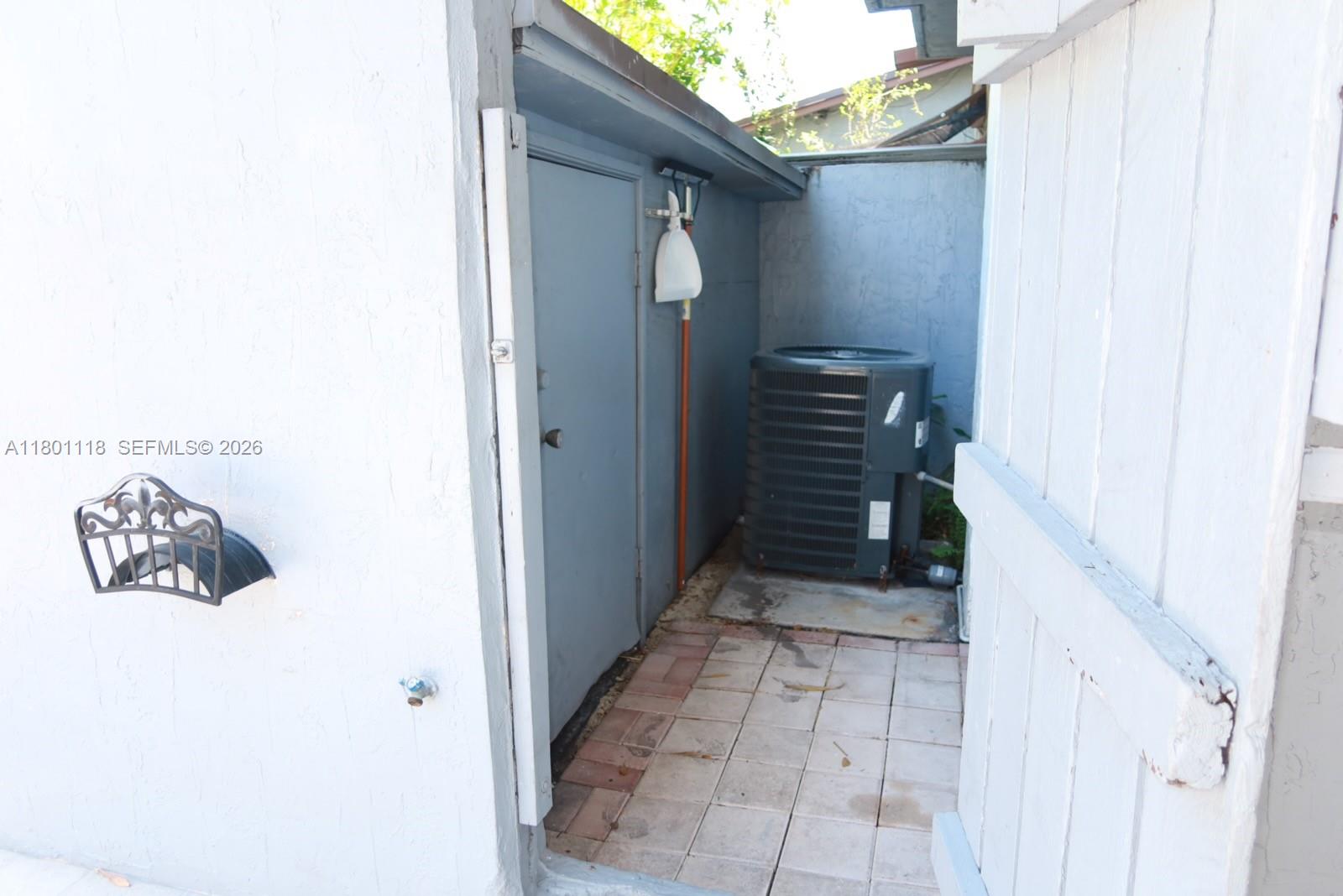 An outdoor utility area features a gray door, an air conditioning unit, and tiled flooring — 8098 NW 99th Ter, Hialeah Gardens FL 33016, HIALEAH GARDENS, FL