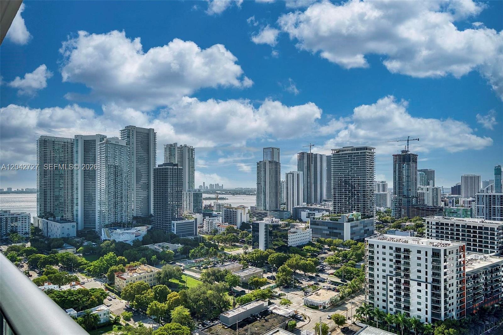 A high-angle view of a dense city skyline with numerous skyscrapers and lush green trees — 121 NE 34th St # 2502, Miami FL 33137, MIAMI, FL